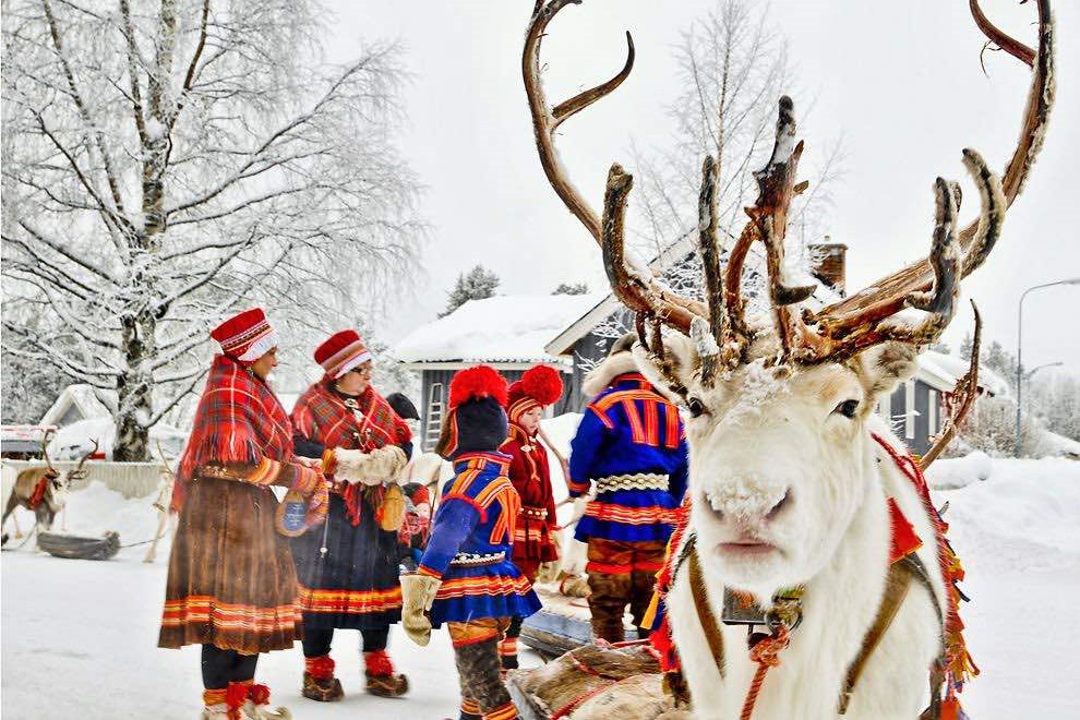 Een groep mensen in traditionele kleding staat naast een rendier, wat het culturele erfgoed en de verbinding met de natuur benadrukt.